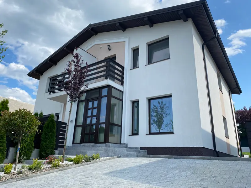 Fațada casei duplex din La Brazi Residence, Bucium: intrarea cu verandă vitrată și balconul de la etaj